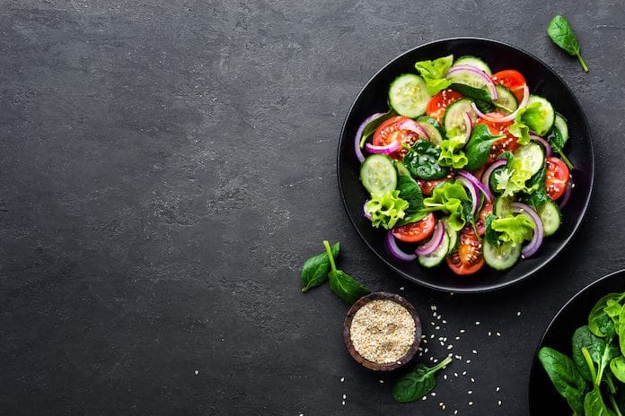 Healthy vegetable salad of fresh tomato, cucumber, onion, spinach, lettuce and sesame on plate. Diet menu. Top view.