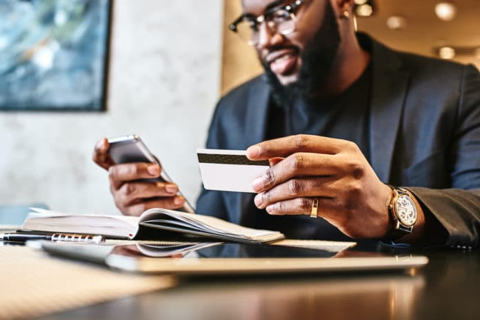 Shot of african american businessman holding mobile and credit card, while resting in the cafe